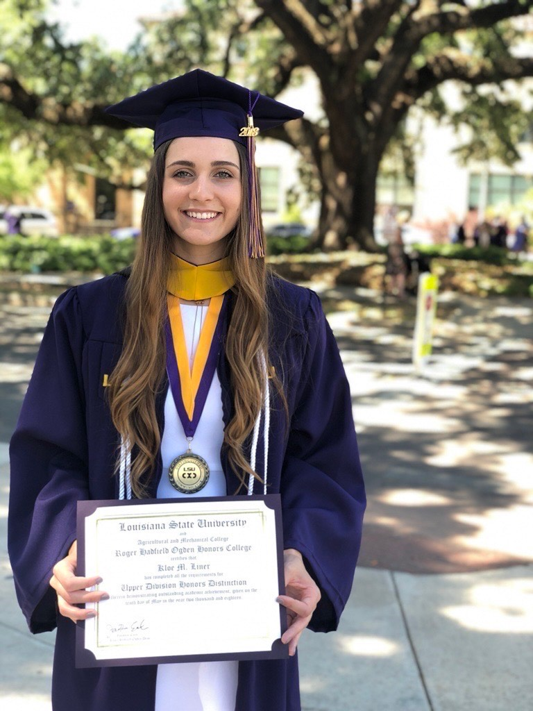 Kloe, younger, dressed in graduation regalia and holding up her diploma.